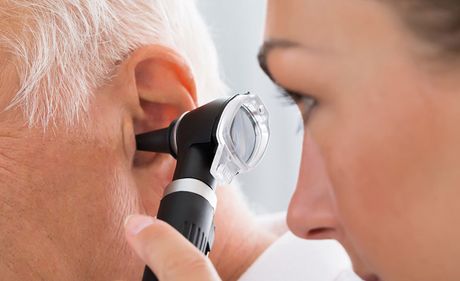 Un médico examina el oído de un paciente mayor con un otoscopio. Están en el interior, con una vista de cerca del procedimiento.