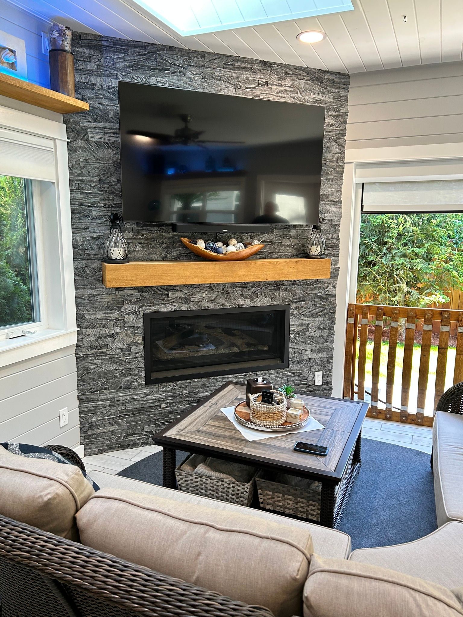 Living room with gray stone fireplace, TV, and wooden mantel; wicker couch, square coffee table.