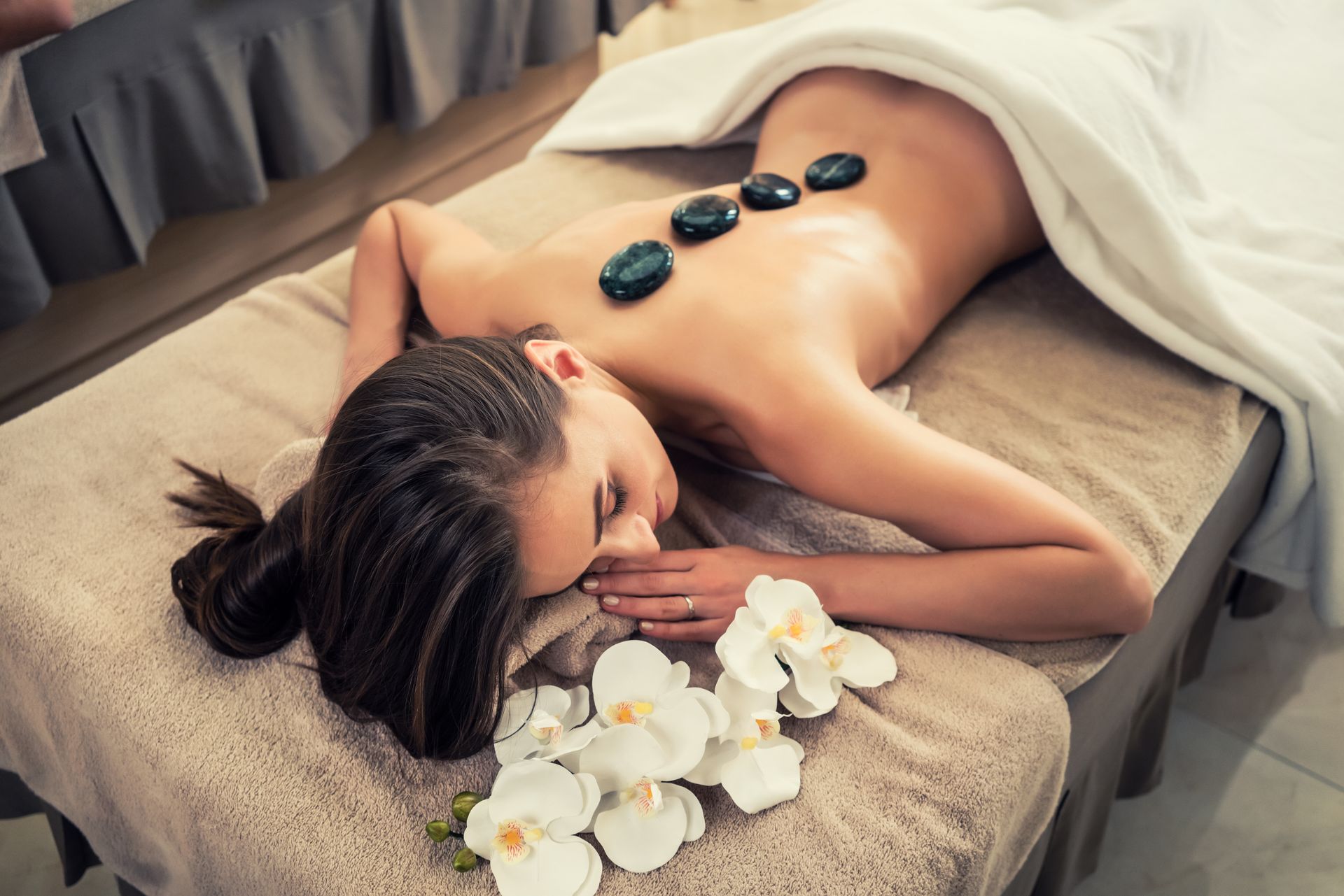 A woman is laying on a massage table with rocks on her back.