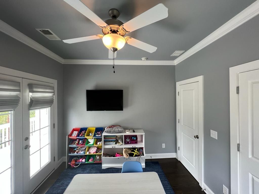 A room with a ceiling fan , television , table and chairs.