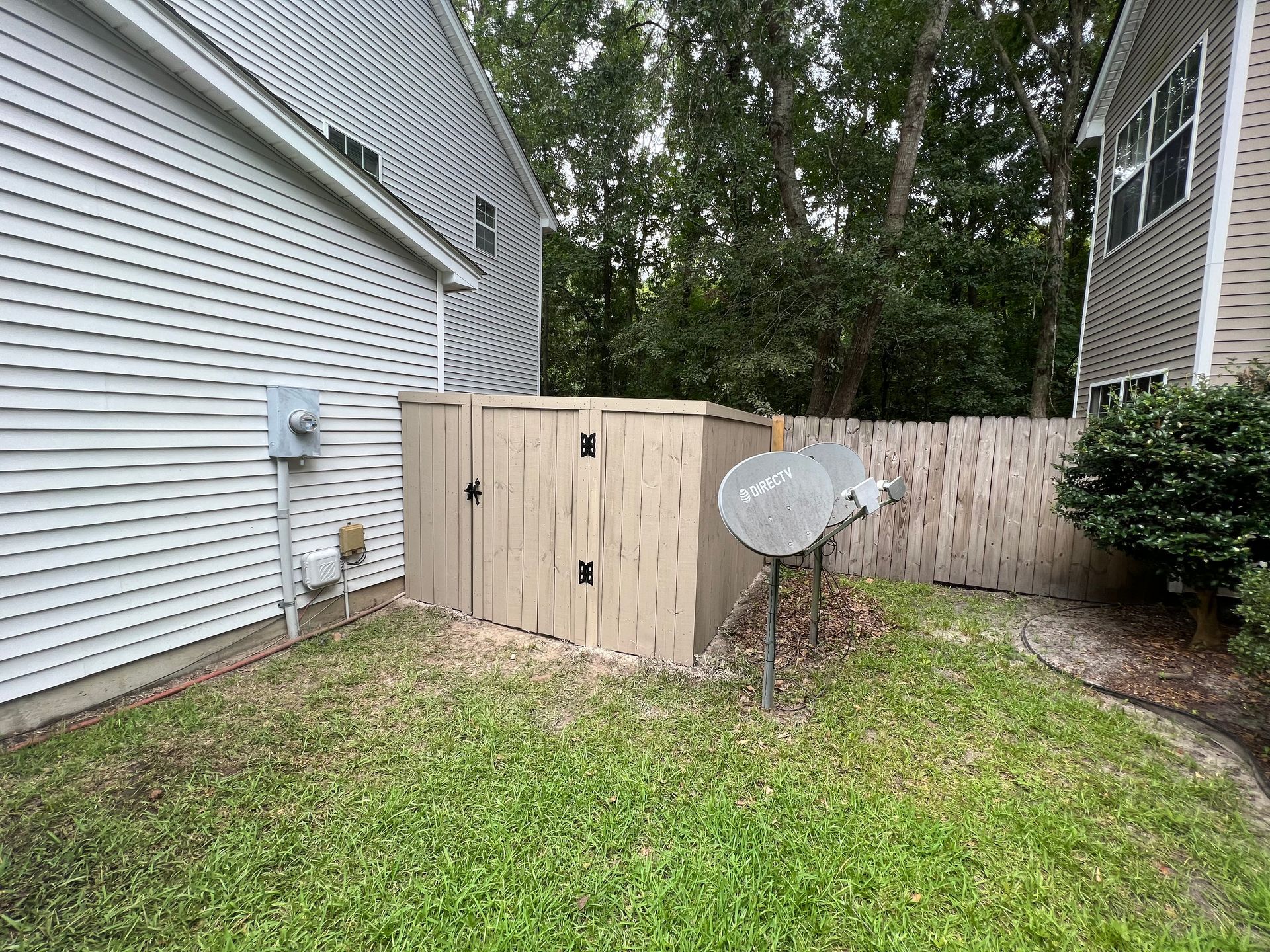 There are two satellite dishes in the backyard of a house.