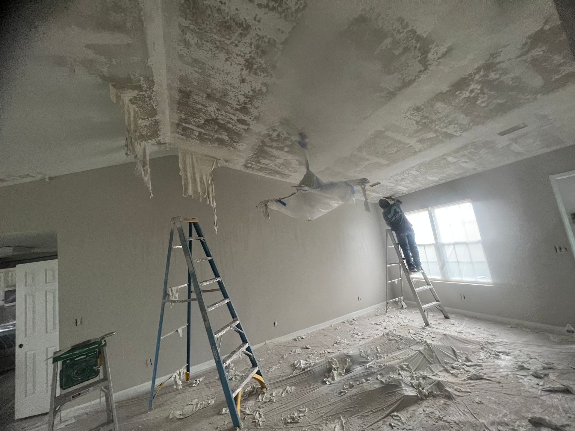 A man is standing on a ladder in a living room.