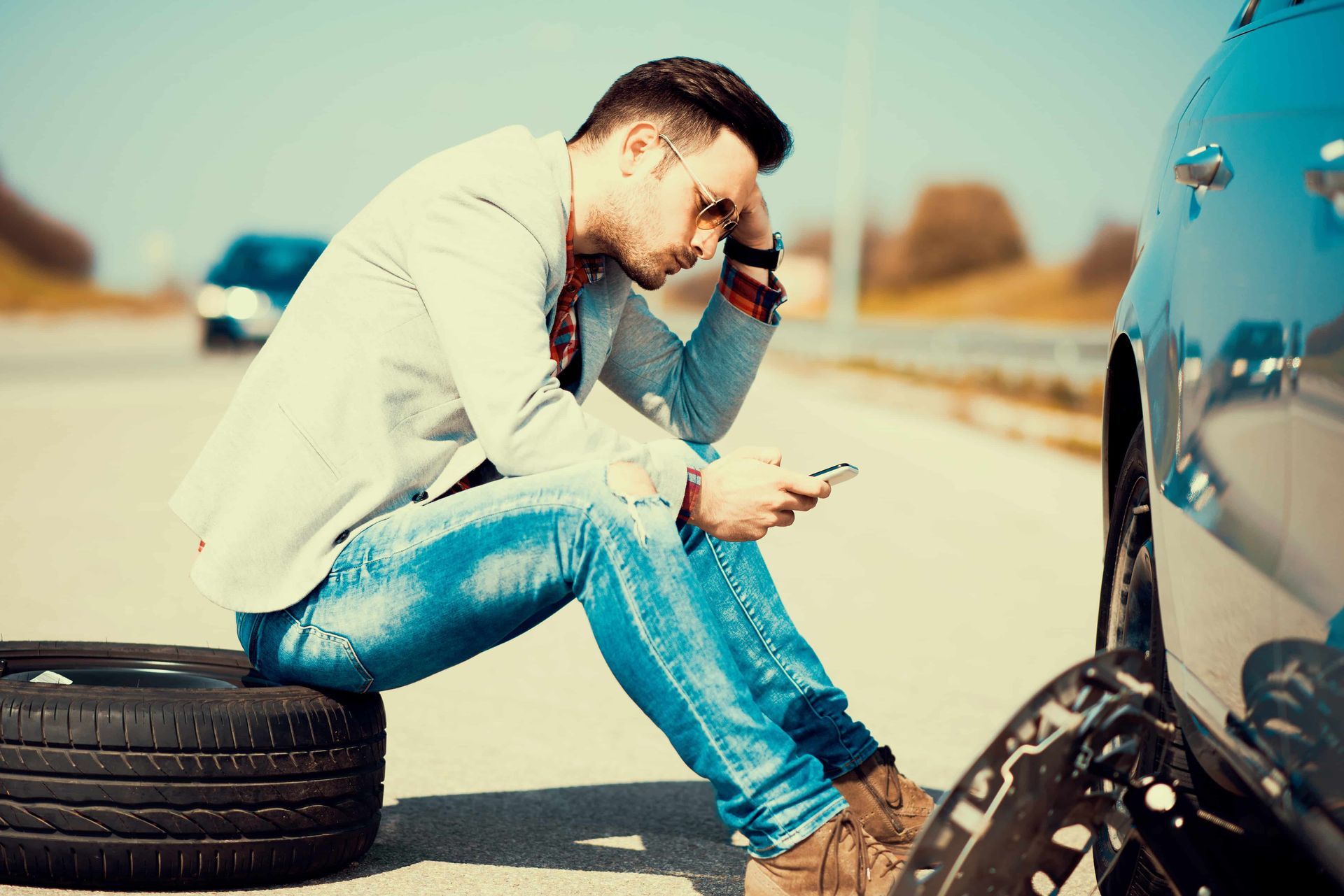 a man sitting on a tire looking for roadside assistance