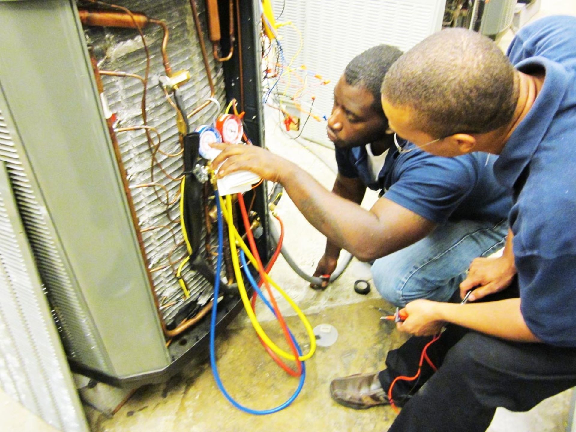 Two men are working on an air conditioner with hoses attached to it