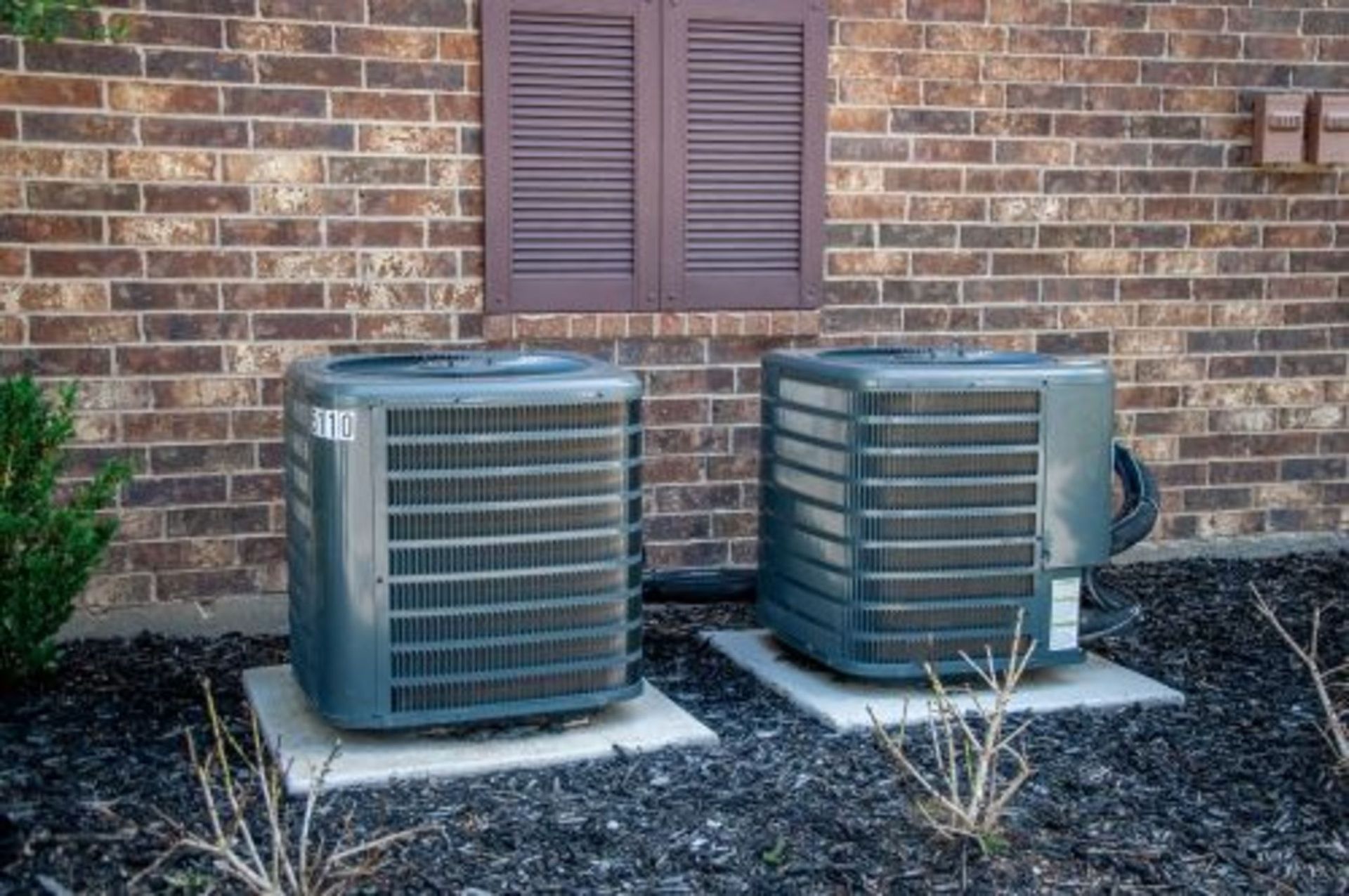 Two air conditioners are sitting outside of a brick building.
