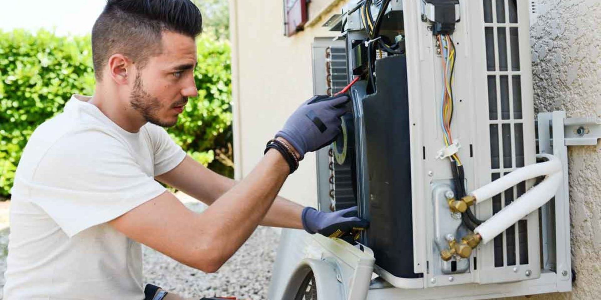 A man is working on an air conditioner outside of a building.