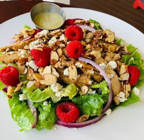 A white plate topped with a salad with raspberries and chicken