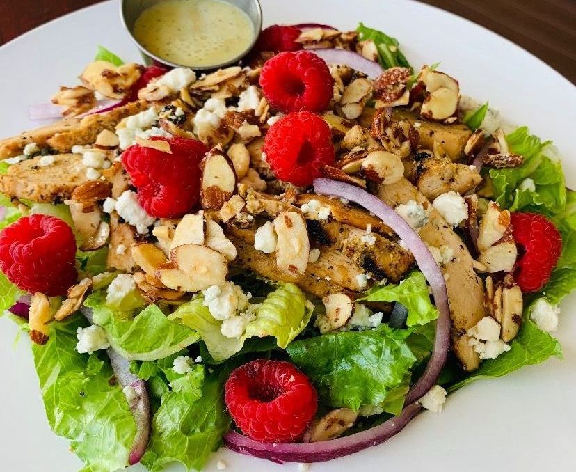 A salad with chicken , raspberries , onions and blue cheese on a white plate.