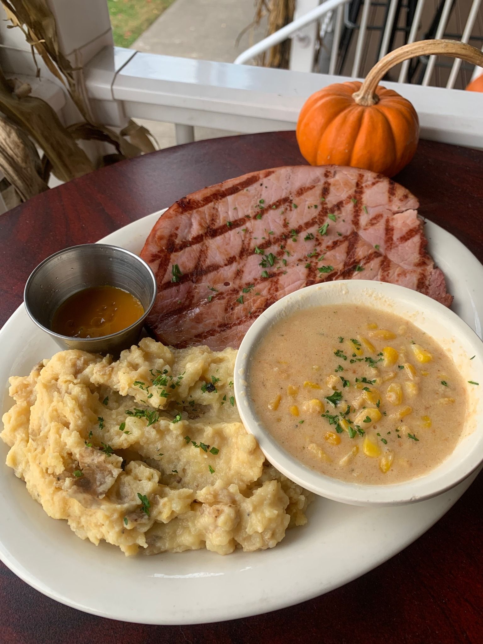 A plate of food with mashed potatoes , corn chowder and ham on a table.