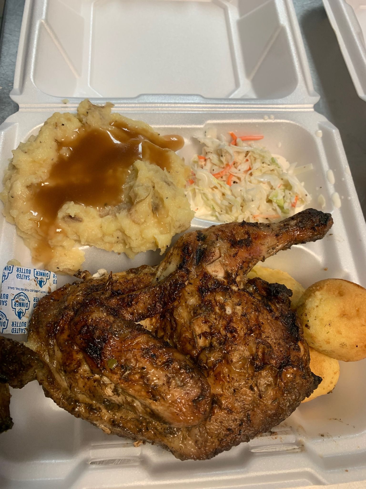 A styrofoam container filled with chicken , mashed potatoes , coleslaw and gravy.