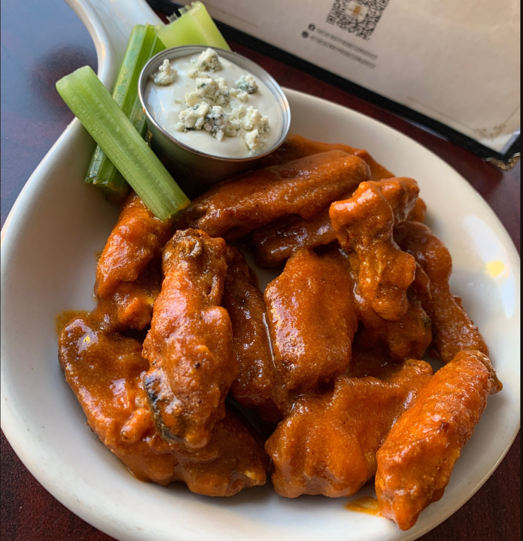 A bowl of chicken wings with celery and blue cheese sauce
