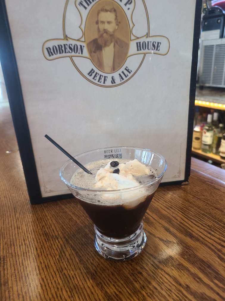 A martini with ice cream in it is sitting on a wooden table.