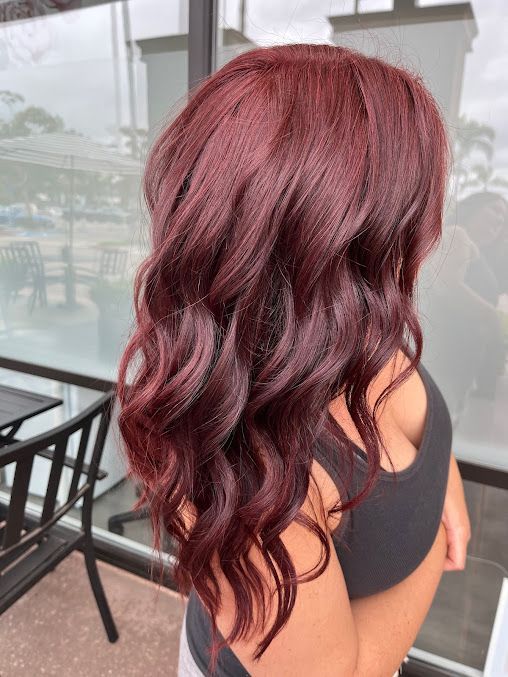 A woman with long red hair is standing in front of a window.