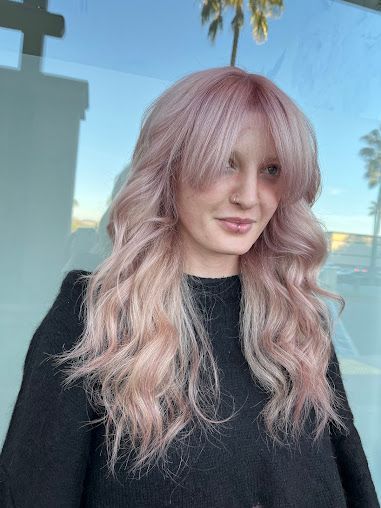 A woman with long pink hair and bangs is wearing a black sweater.