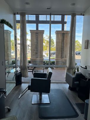 A salon with a chair , sink , mirror and large windows.