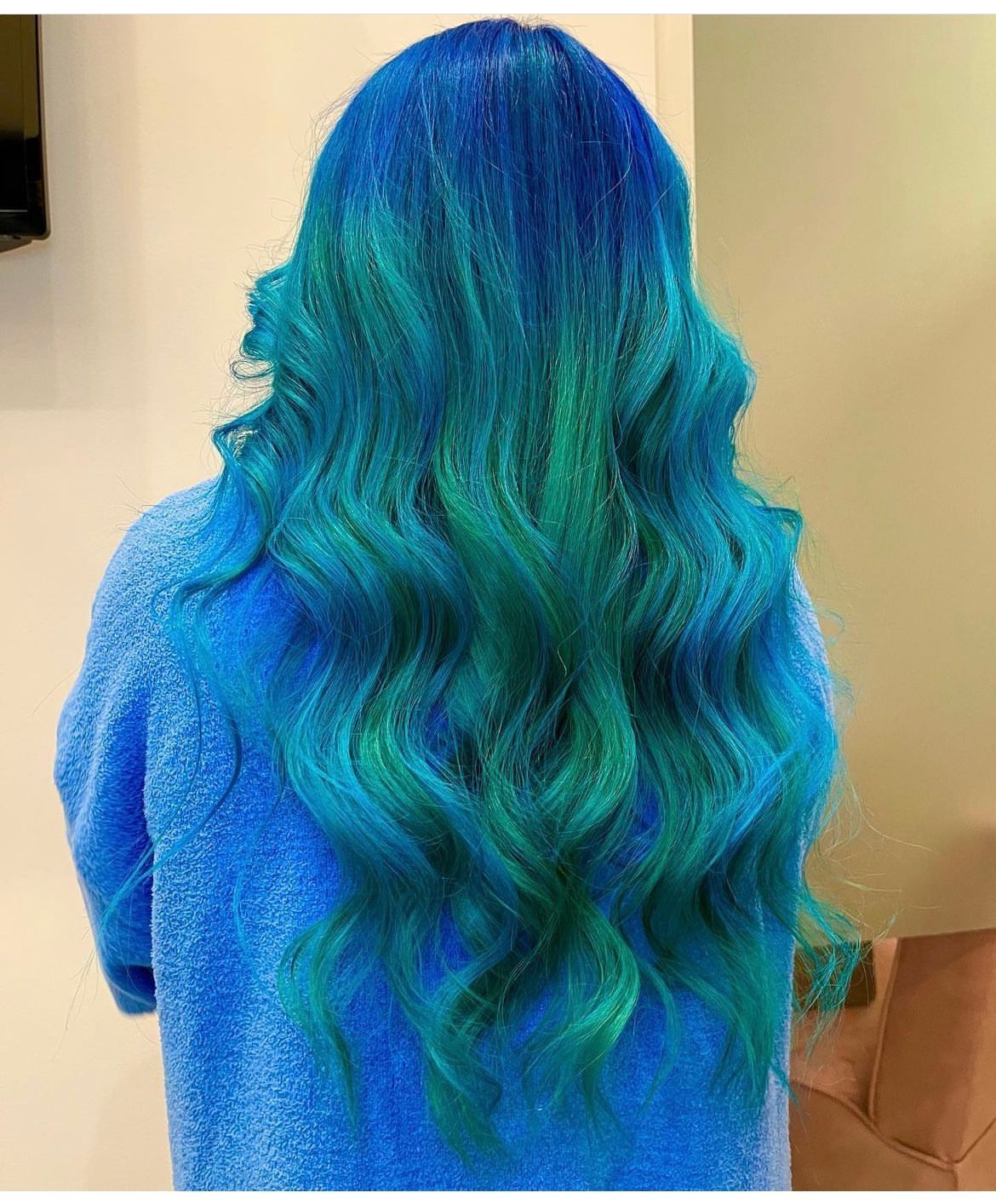 A woman with blue and green hair is wearing a blue sweater.