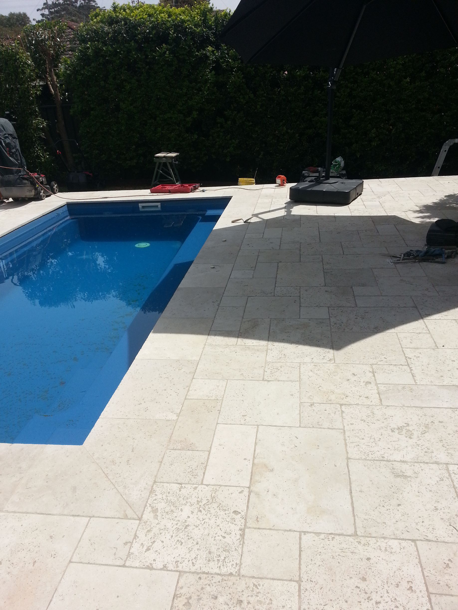 A large swimming pool surrounded by white tiles and a black umbrella — South Coast Flooring in Berkeley, NSW