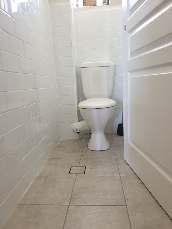 A white toilet is sitting in a bathroom next to a door — South Coast Flooring in Berkeley, NSW