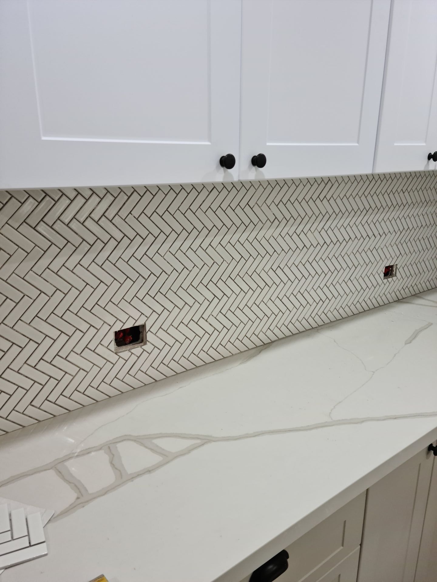 A kitchen with white cabinets and a white counter top with a herringbone tile backsplash — South Coast Flooring in Berkeley, NSW