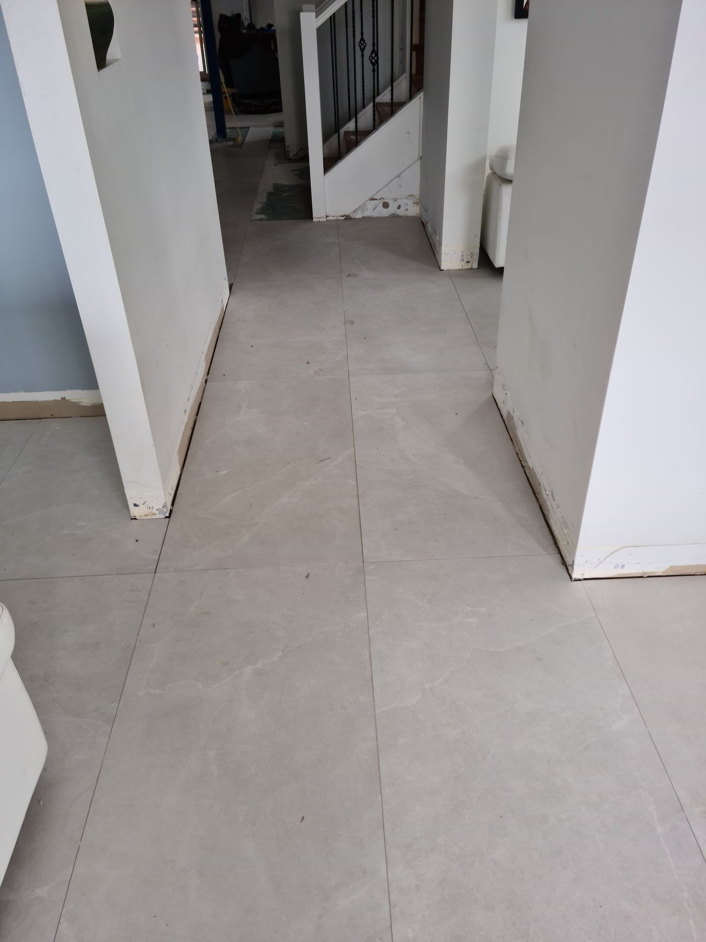 A hallway with tile floors and white walls leading to a staircase.