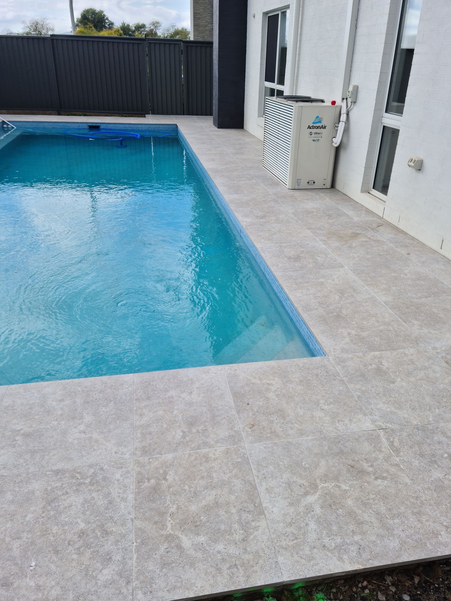 A large swimming pool with a tiled patio in front of a house — South Coast Flooring in Berkeley, NSW