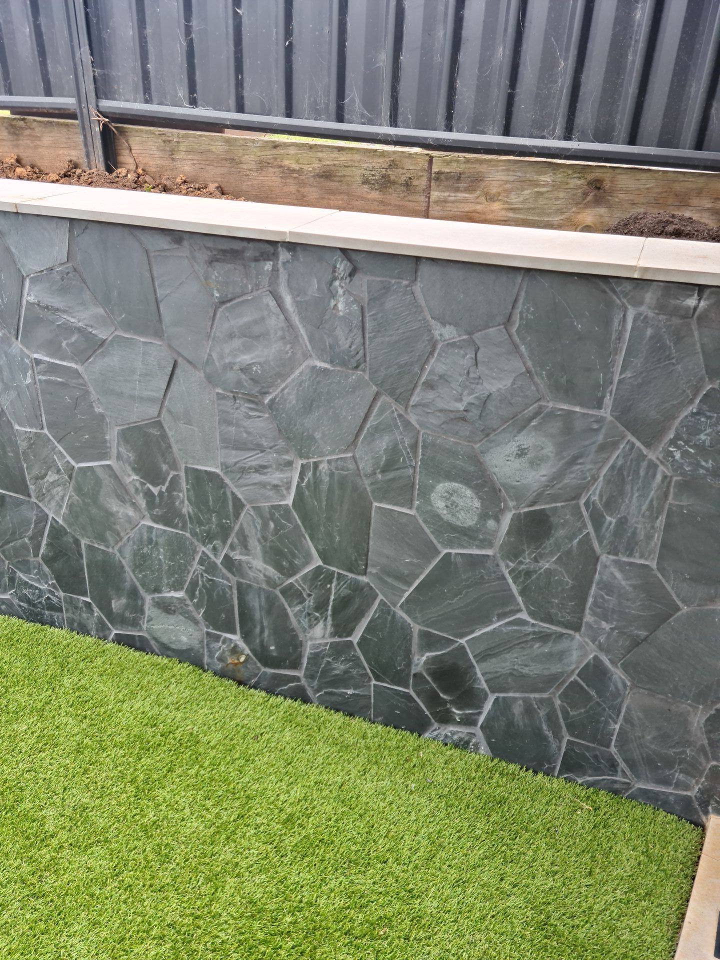 A stone wall with a fence in the background and grass in the foreground — South Coast Flooring in Berkeley, NSW