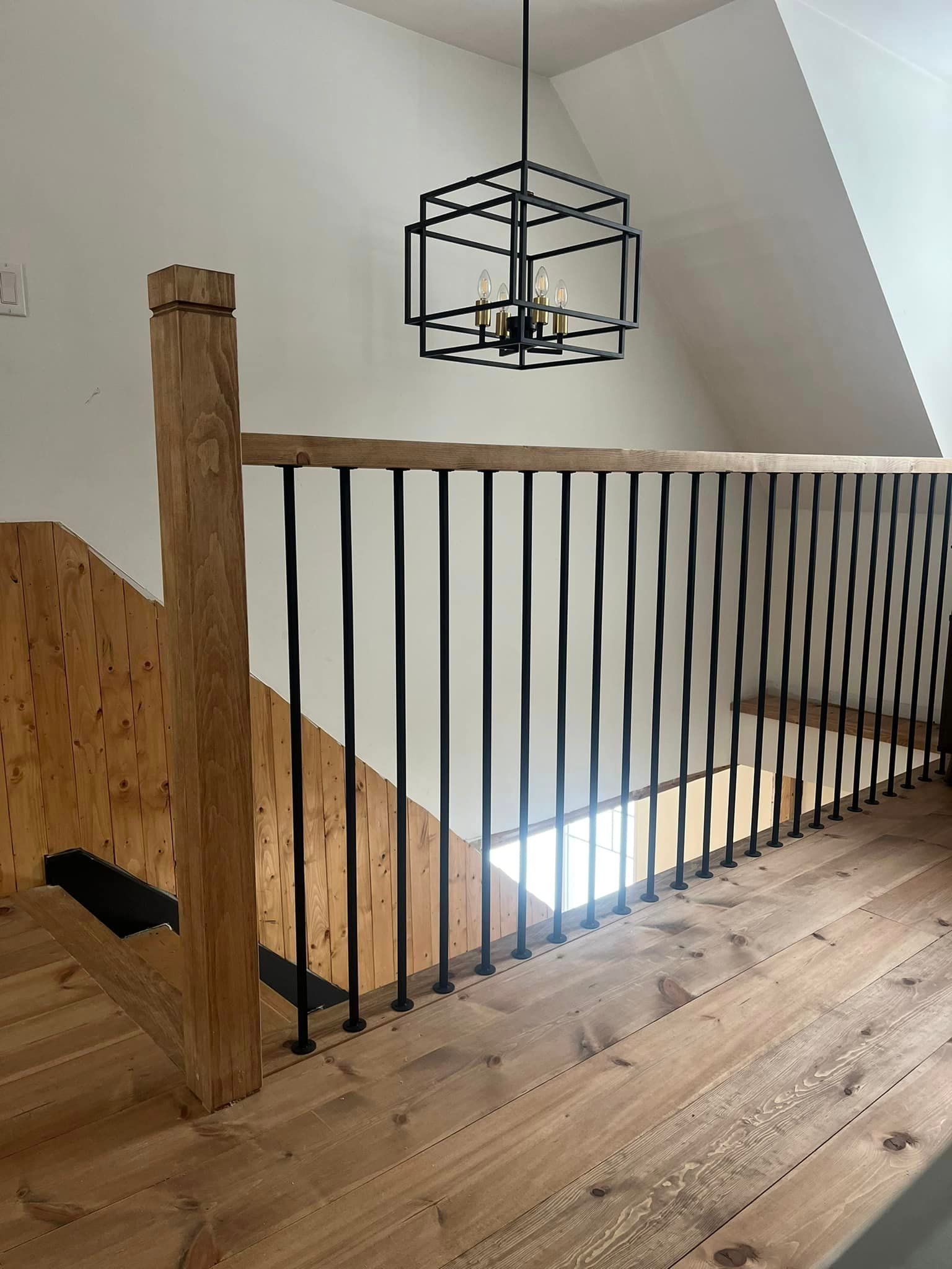 Un escalier en bois avec une rampe en métal et un lustre suspendu au plafond.
