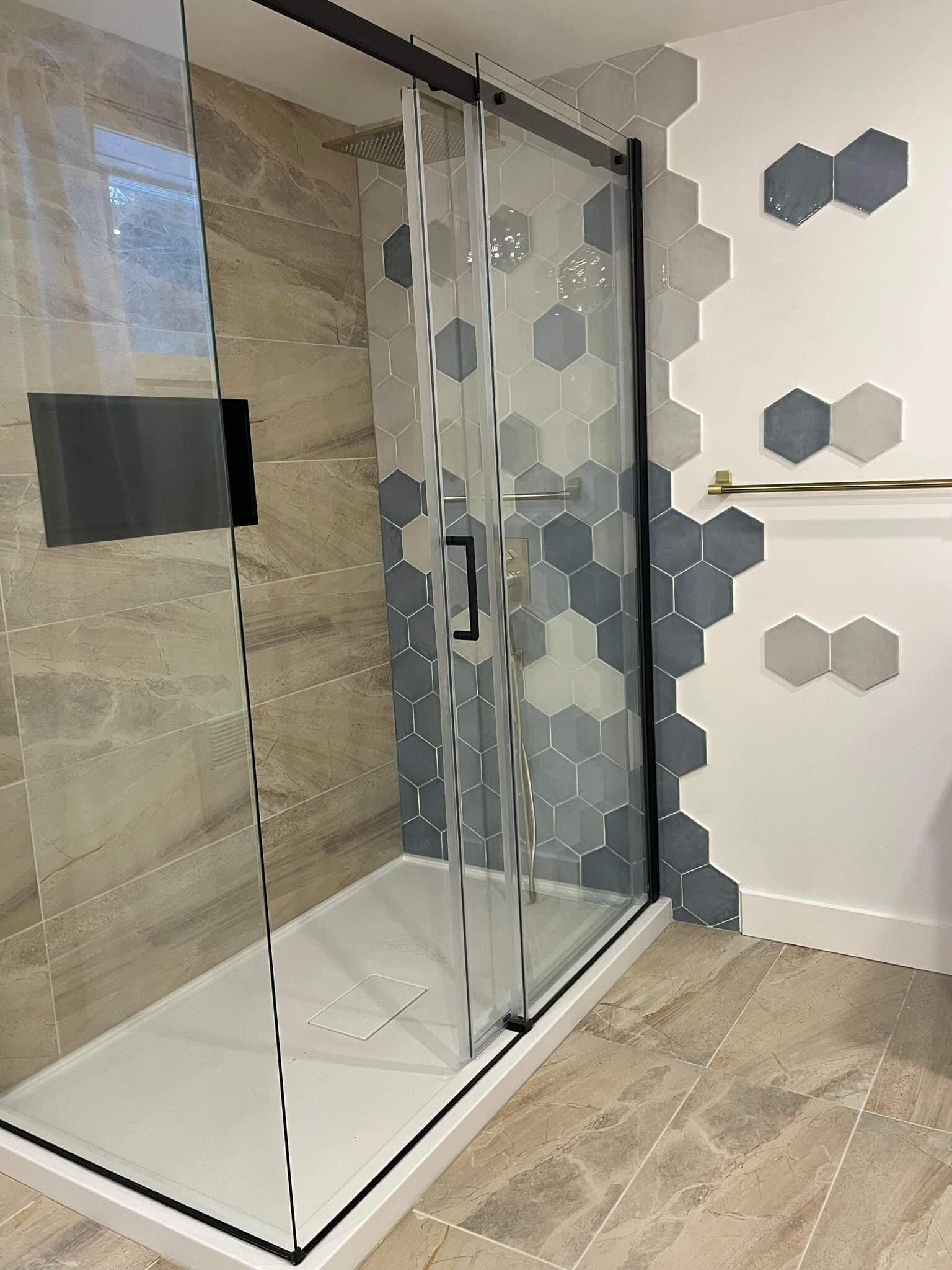 Une salle de bain avec une cabine de douche et des carreaux hexagonaux au mur.