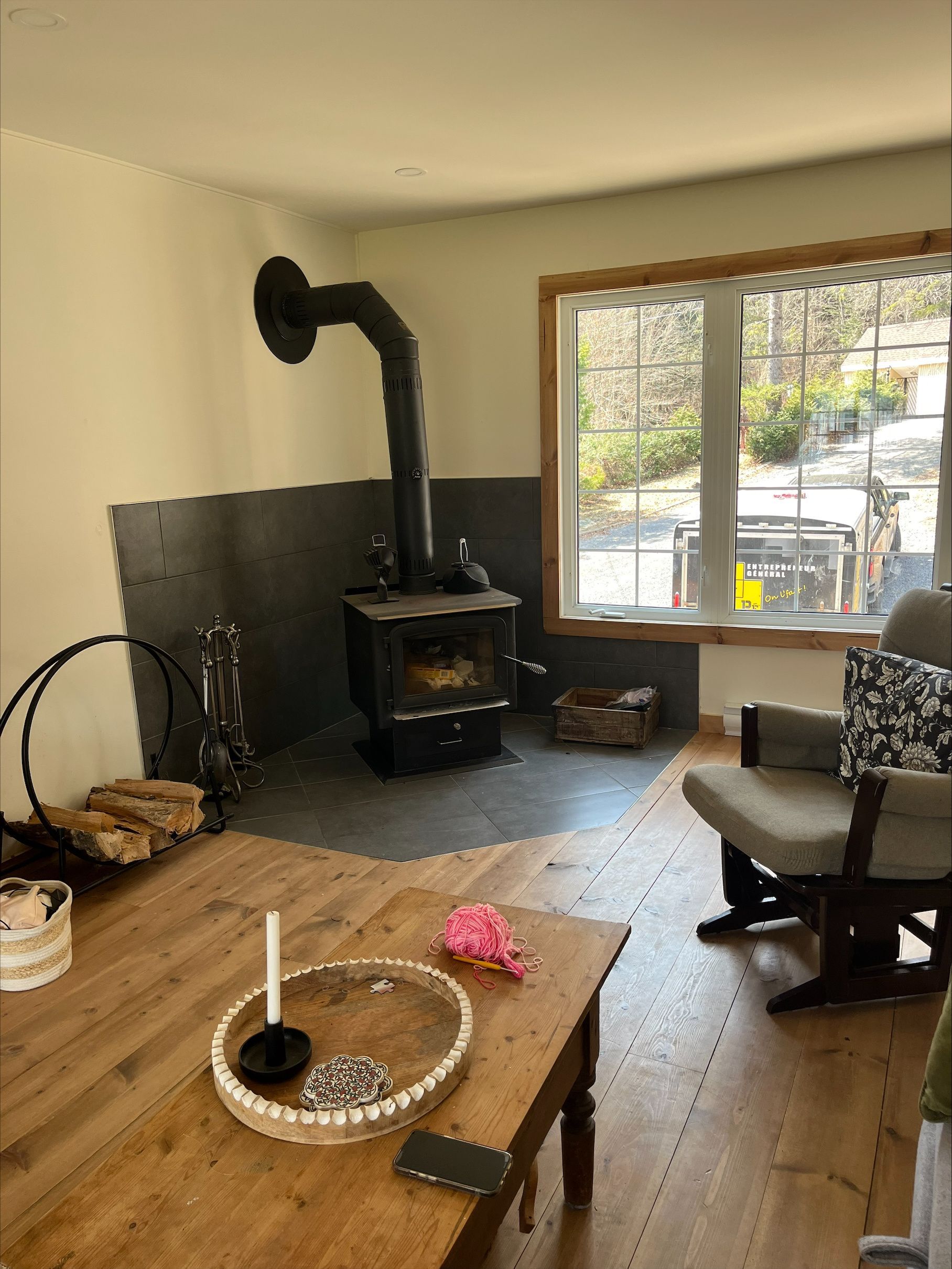 Un salon avec un poêle à bois, une table, une chaise et une fenêtre.