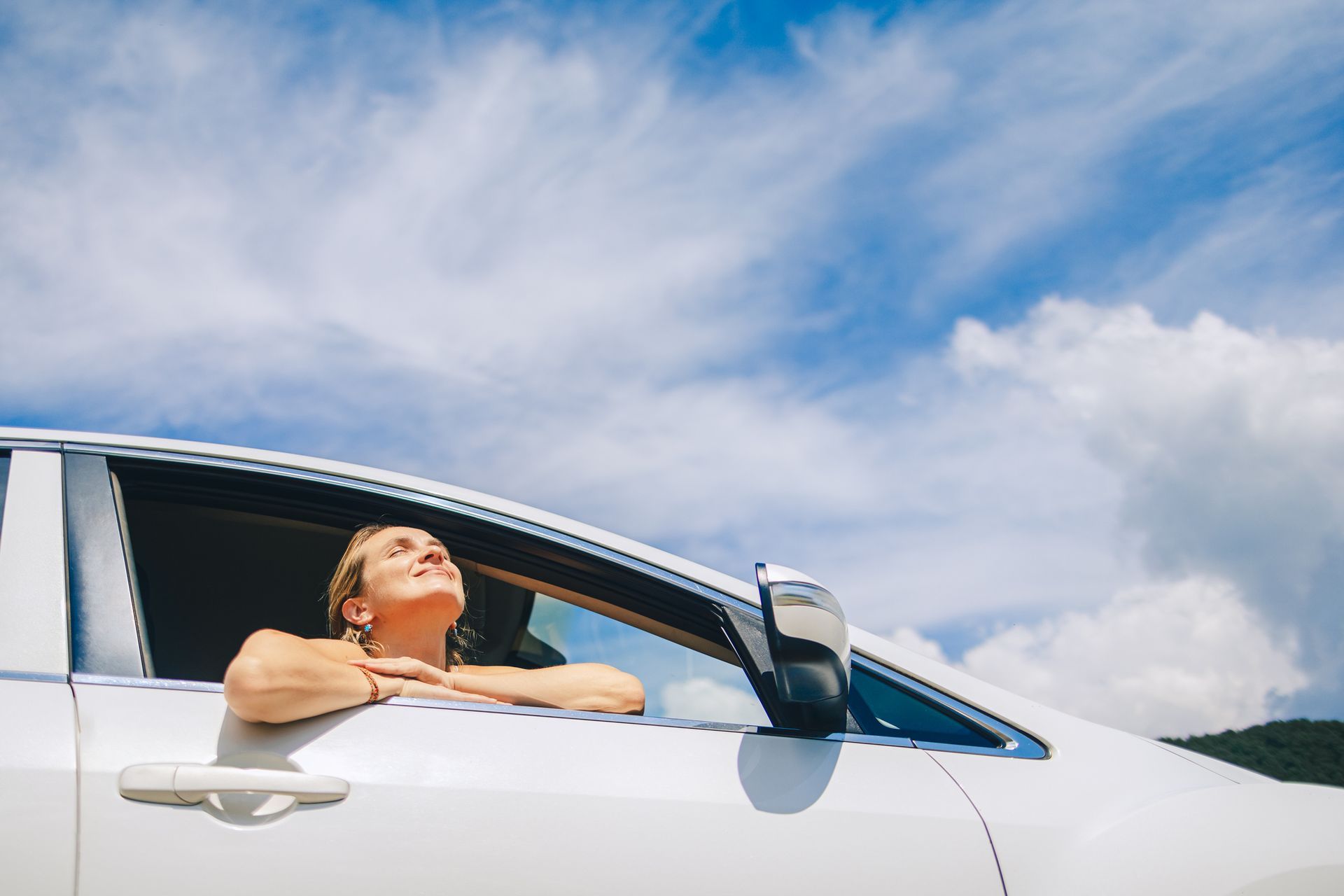 View of a Woman Smiling to the Sun From a Car Seat Against a Blue Sky View of a Woman Smiling to the Sun From a Car Seat Against a Blue Sky
