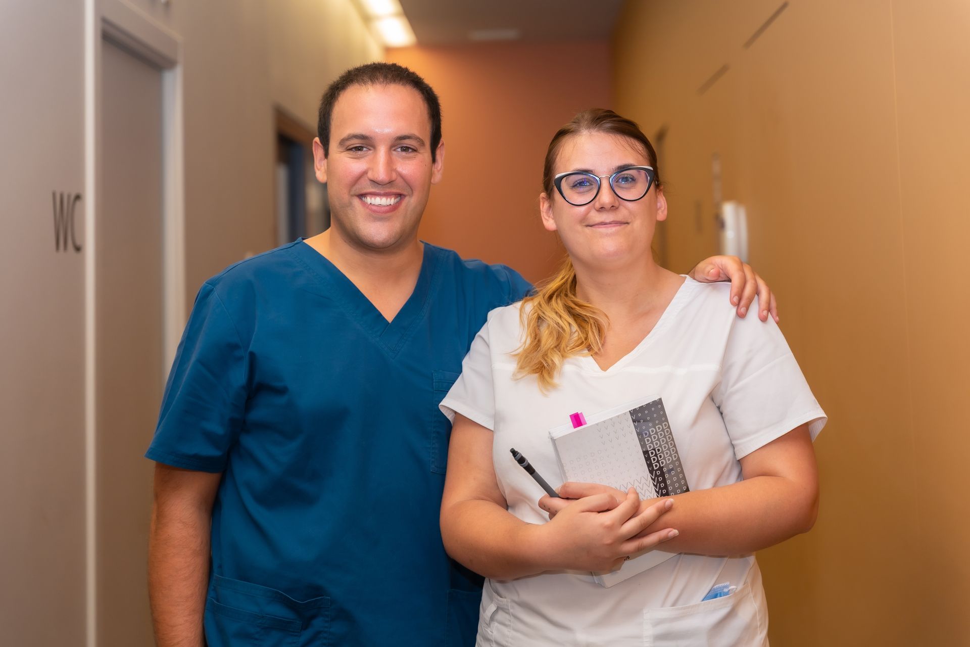 Deux professionnels de la santé souriants dans un couloir, l'un avec le bras autour de l'autre.