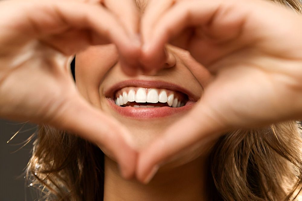 Femme souriante, formant une forme de cœur avec ses mains, mettant en valeur ses dents blanches.facette