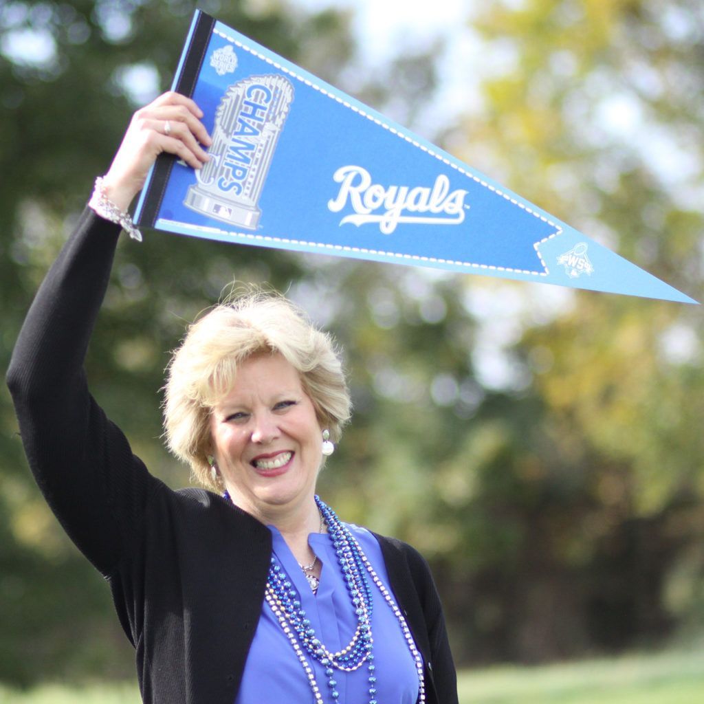 A Kari Simpson is holding up a blue royals pennant