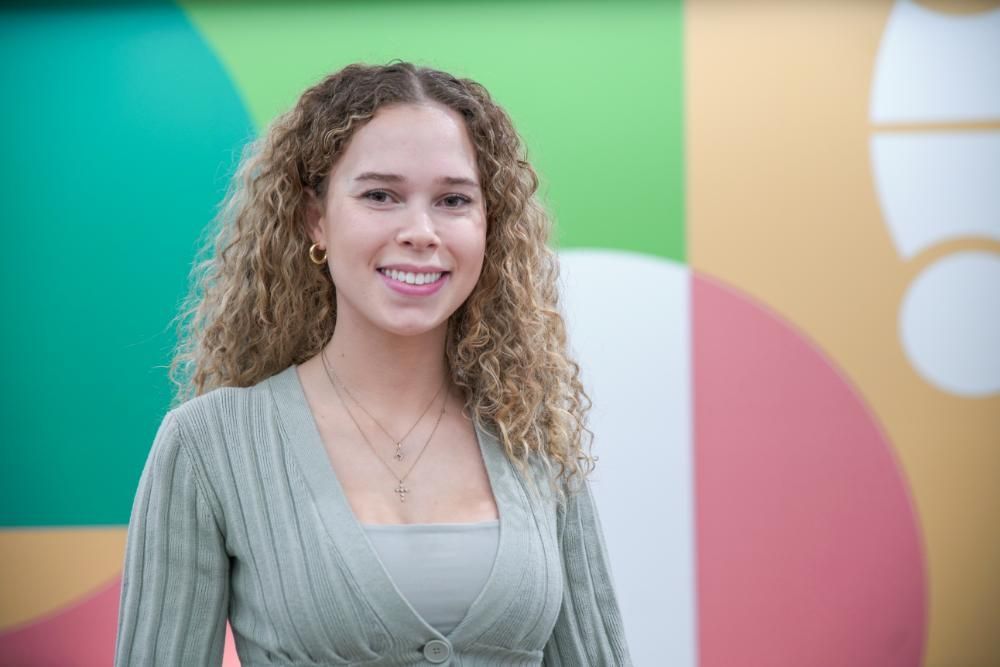 A woman with curly hair is smiling and wearing a white shirt.