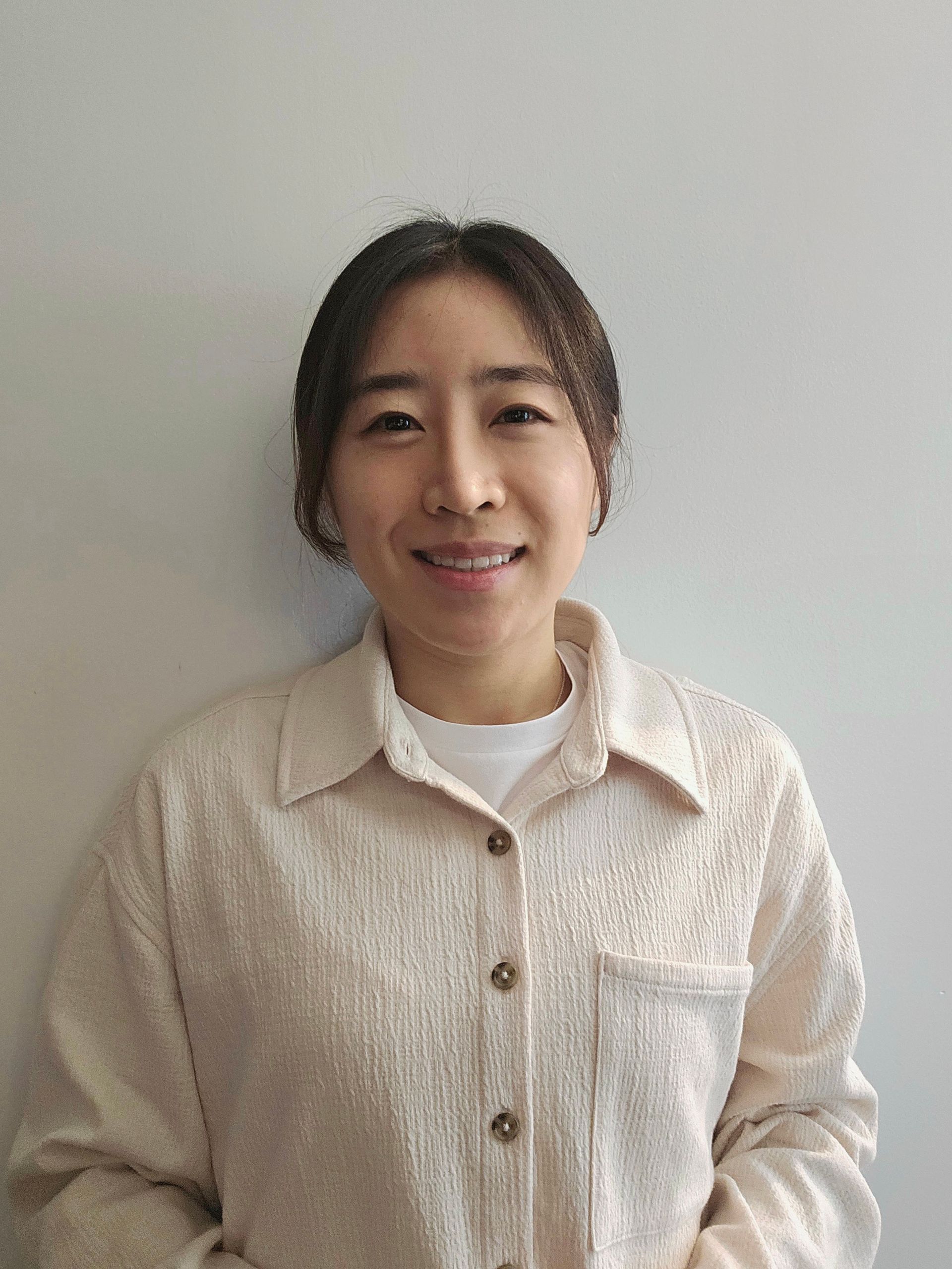 A woman with curly hair is smiling and wearing a white shirt.