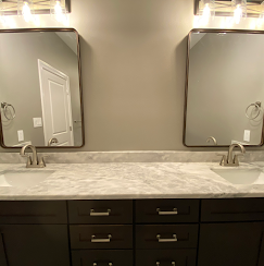 Bathroom with two mirrors over sinks, grey walls, dark cabinets, and marble countertop.