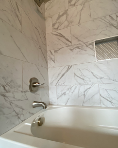 White marble tile in a bathroom with tub and brushed nickel faucet.