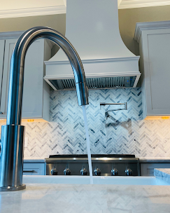 Kitchen faucet with water running, in front of a stove and backsplash.