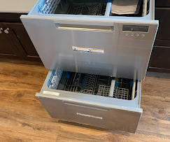 Stainless steel, two-drawer dishwasher with both drawers open on a wooden floor.