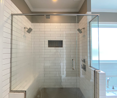 Glass-enclosed shower with white subway tile walls, two shower heads, and a built-in recessed storage niche.