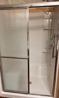White shower stall with sliding glass door, chrome frame, and built-in shelves.