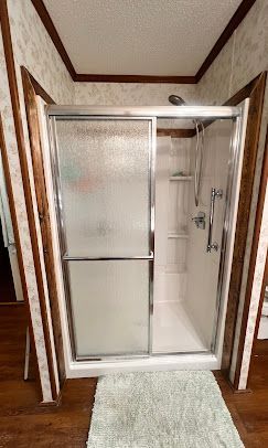 Shower stall with frosted glass doors and wood trim, set on a wood floor with a rug.