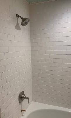 White tiled shower with showerhead, faucet, and tub.