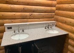Bathroom vanity with two sinks, granite countertop, and log cabin walls.