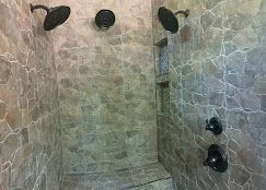 Shower with stone tile walls, three showerheads, and a built-in bench. Dark fixtures and neutral color scheme.