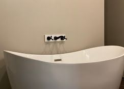 White freestanding bathtub below black faucet fixtures on a beige wall.