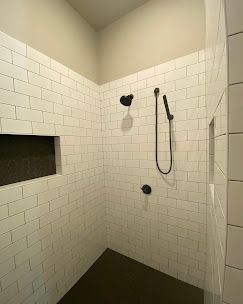 White-tiled shower with dark fixtures and built-in niches. Dark floor.