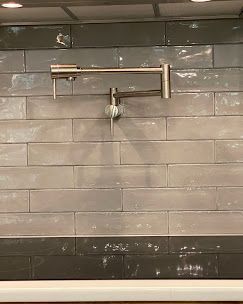 Pot filler faucet on a gray and black tiled backsplash.