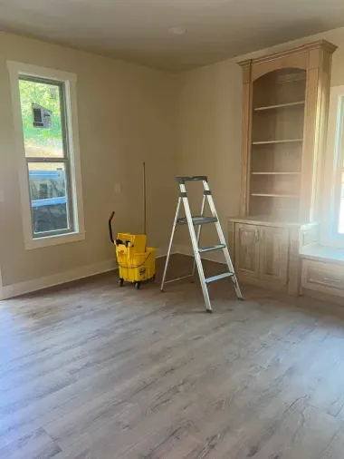 Empty room with wood-look flooring, built-in shelving, a window, and a ladder. A yellow machine sits on the floor.
