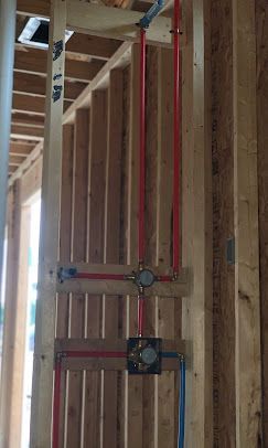 Plumbing pipes and fixtures in a wooden wall. Red and blue PEX pipes, brass valves, and a gray pipe.